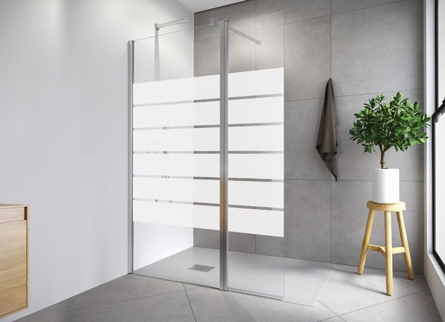 Ducha moderna con panel de vidrio esmerilado y baño en tonos neutros con planta y taburete.