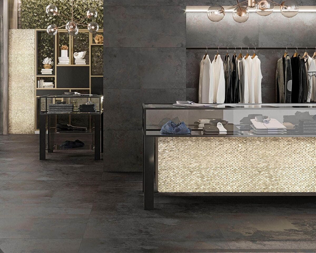 Interior de tienda de ropa con mostradores de exhibición metálicos, estantes de ropa e iluminación ambiental.