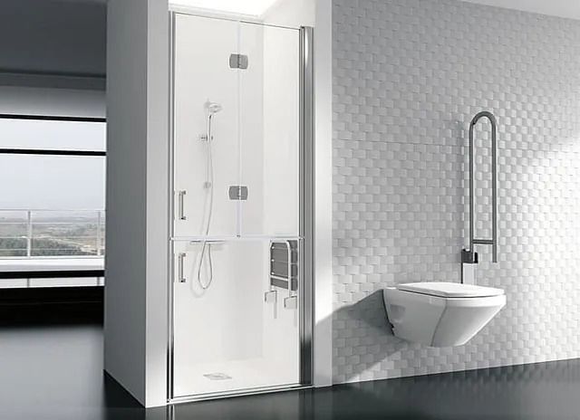 Baño accesible con ducha de cristal, barra de apoyo e inodoro montado en la pared.