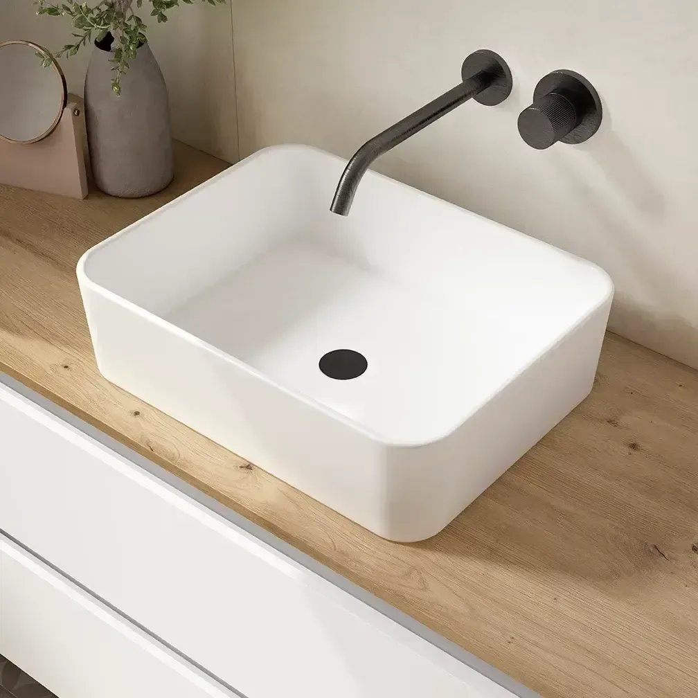 Lavabo de baño rectangular blanco con grifo y desagüe negros sobre encimera de madera.