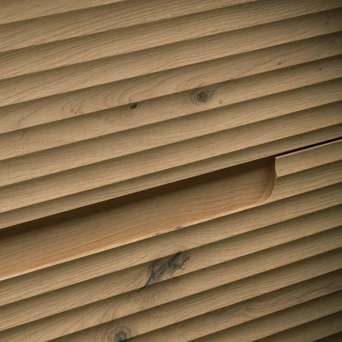 Cajón de madera con lamas horizontales estriadas y tirador redondeado.