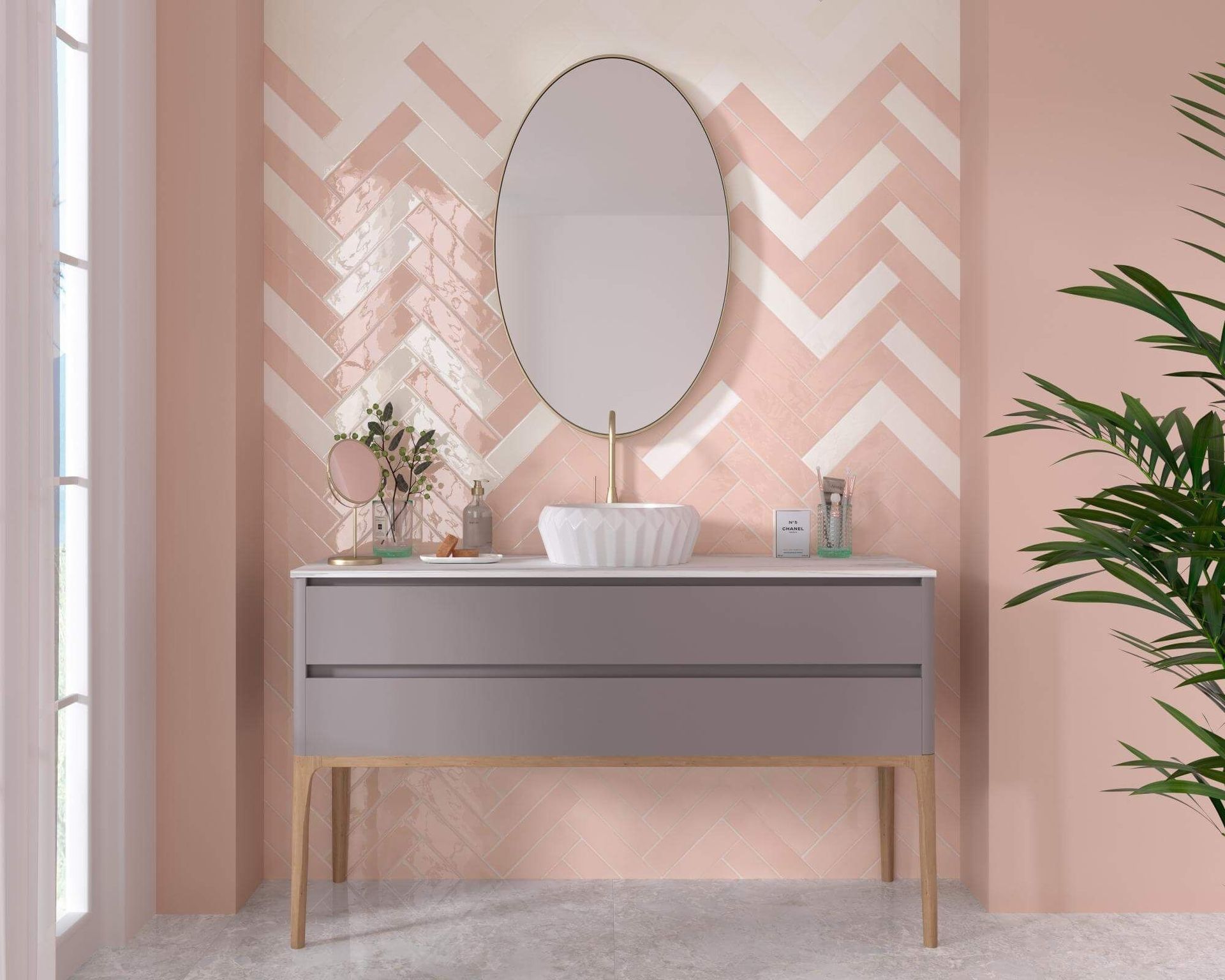 Baño con azulejos de espiga rosa y blanco, tocador gris y espejo ovalado.
