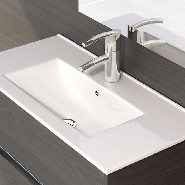 Lavabo de baño con grifo cromado sobre encimera blanca, mueble gris oscuro y espejo.