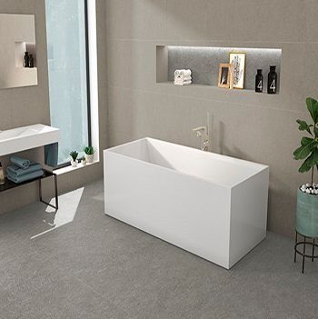 Baño moderno con bañera rectangular blanca, paredes y suelo grises y una planta.