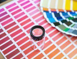 Muestras de color en tonos rosa, rojo y naranja con lupa; otras paletas de colores a la vista.