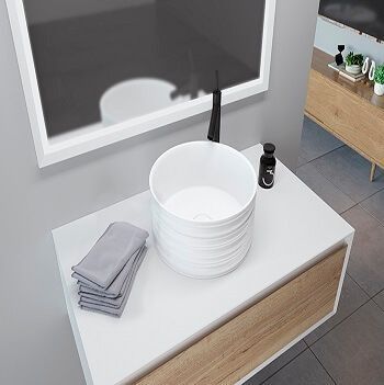 Lavabo blanco sobre mueble blanco y madera en un baño con espejo.