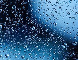 Gotas de agua sobre una superficie azul, reflejando la luz.