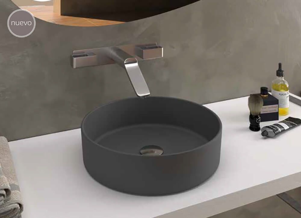 Lavabo de baño circular gris oscuro con grifería moderna, sobre encimera blanca.