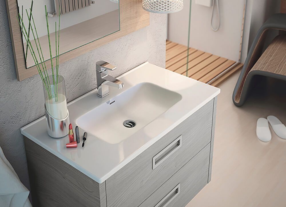 Mueble de baño con encimera blanca, lavabo encastrado, dos cajones y grifería cromada; tocador y jarrón de cañas.