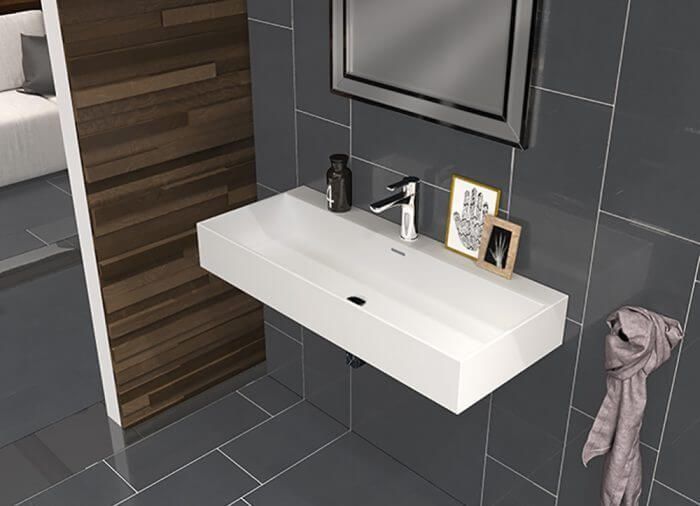 Lavabo de pared moderno de color blanco en un baño con azulejos grises con decoración y toalla.