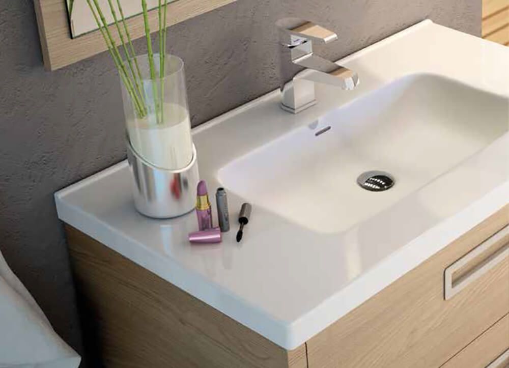 Mueble de baño con encimera blanca, lavabo integrado, grifería cromada y mueble de madera.