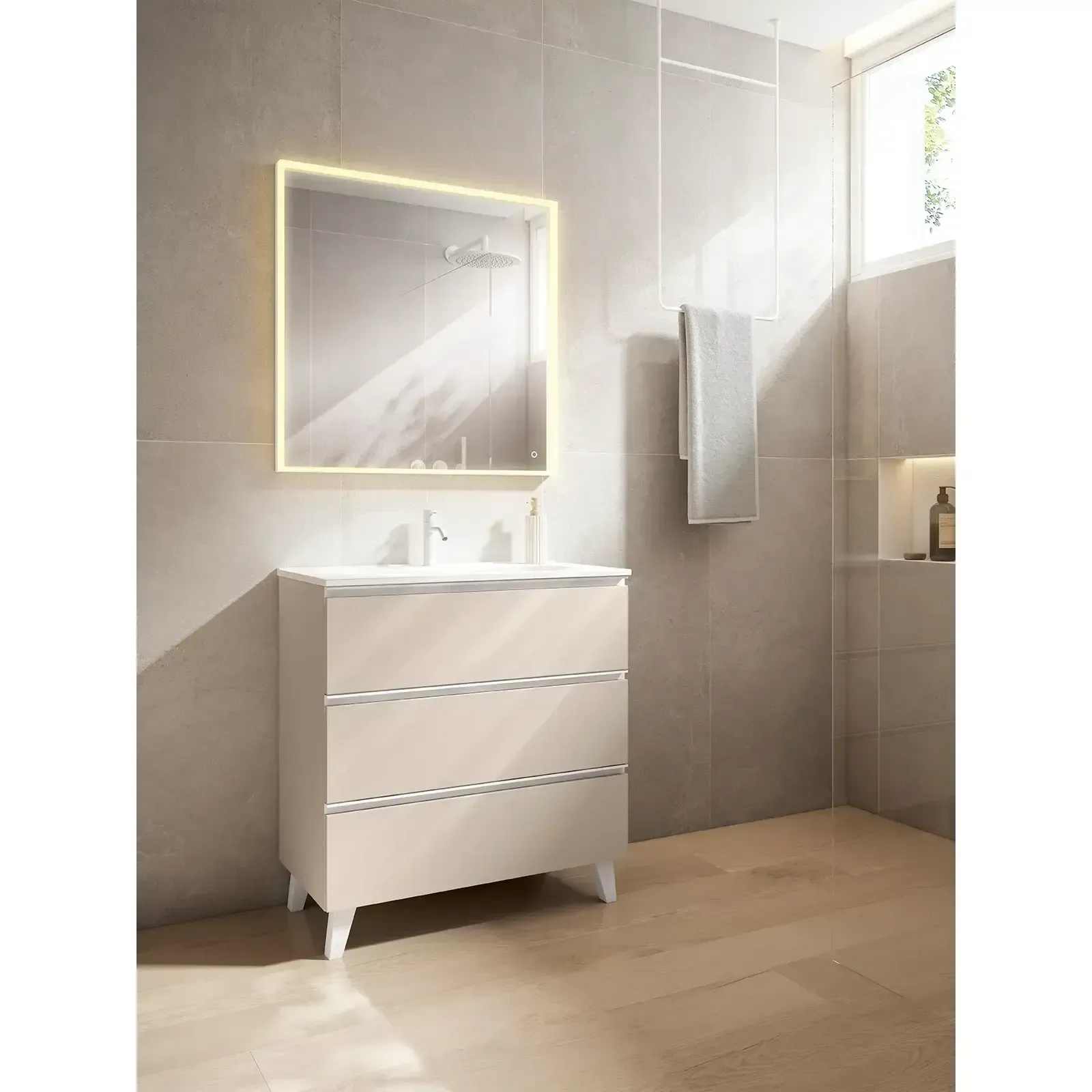 Baño con tocador beige, espejo iluminado y toallero contra una pared de azulejos gris claro.