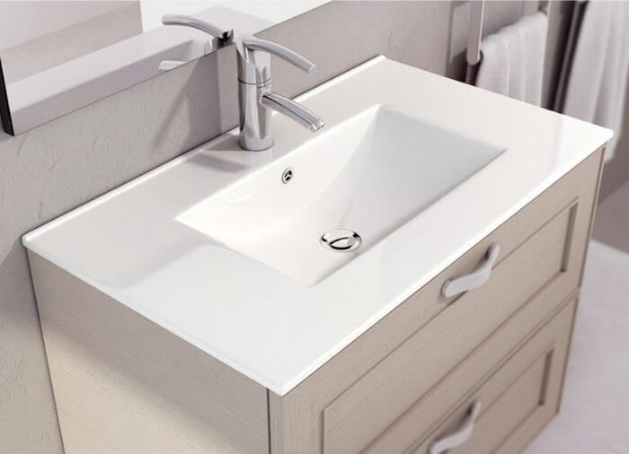 Mueble de baño con encimera blanca, lavabo rectangular, grifería cromada y mueble color tostado con dos cajones.
