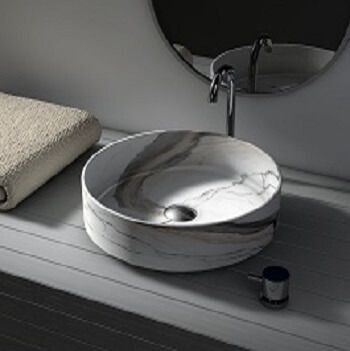 Lavabo redondo con diseño de mármol, con grifo, dispensador de jabón y toallero sobre encimera. Espejo al fondo.