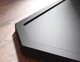 Dispositivo electrónico negro, en ángulo, sobre una superficie de madera con una línea fina y oscura en la parte superior.