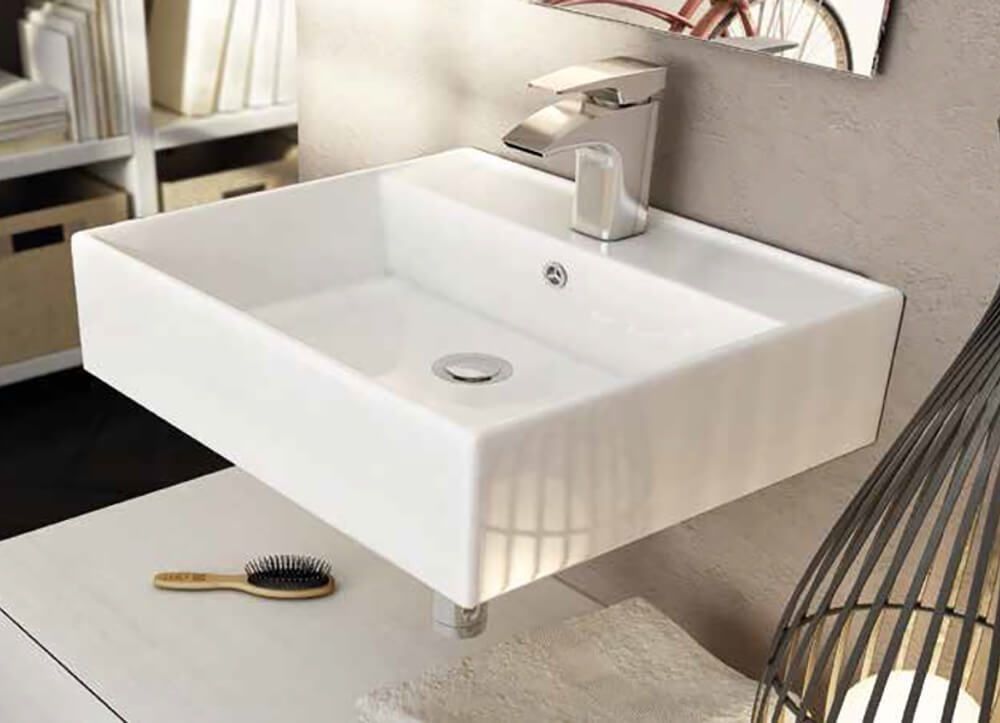 Lavabo de pared rectangular blanco con grifo cromado. Debajo hay un cepillo y una toalla.