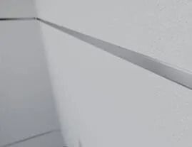 Paredes blancas que se unen en una esquina con una fina tira horizontal de metal.