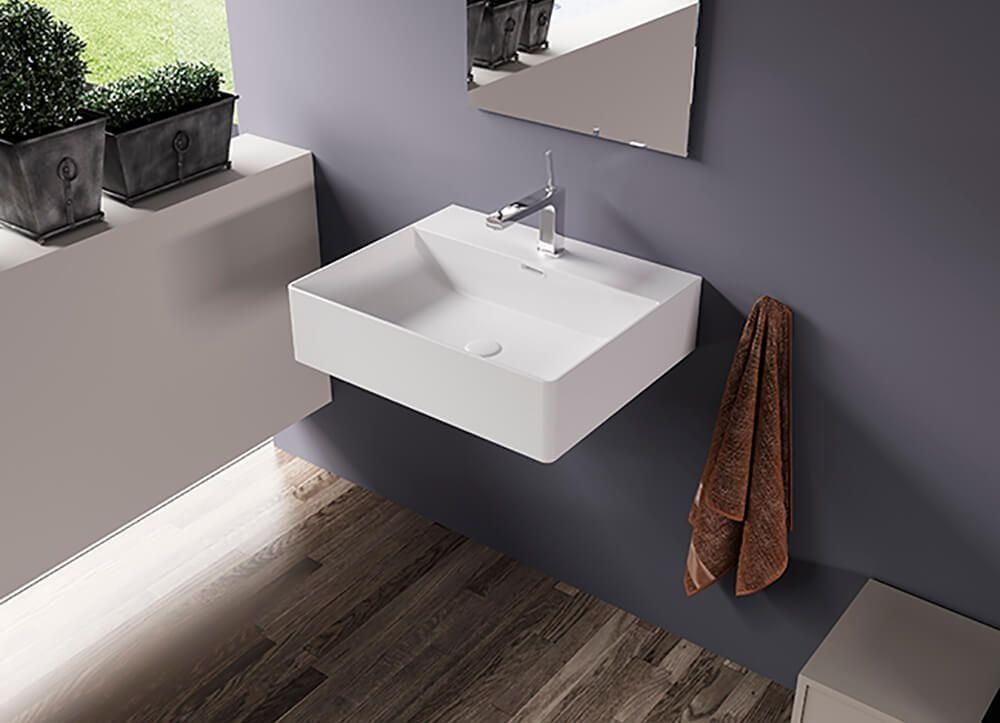 Lavabo de baño cuadrado blanco montado en una pared gris; una toalla marrón cuelga cerca.