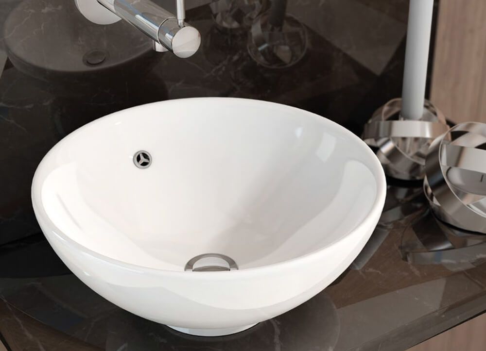 Fregadero redondo de cerámica blanca sobre encimera oscura. Grifo y desagüe cromados visibles.