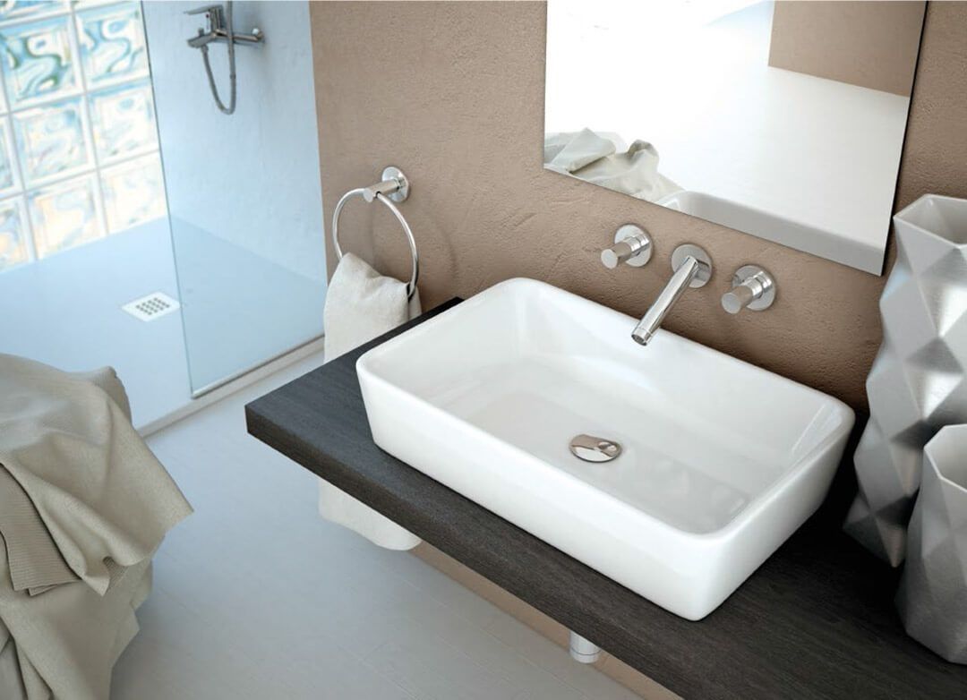 Baño moderno con un lavabo rectangular blanco sobre una encimera de madera oscura, una ducha con ladrillos de vidrio y una pared de color tostado.