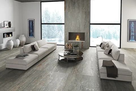 Moderna sala de estar con sofás gris claro, chimenea y grandes ventanales con vistas a un bosque nevado.