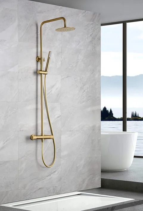 Artefacto de ducha dorado sobre pared de mármol en baño con vista al paisaje y bañera.