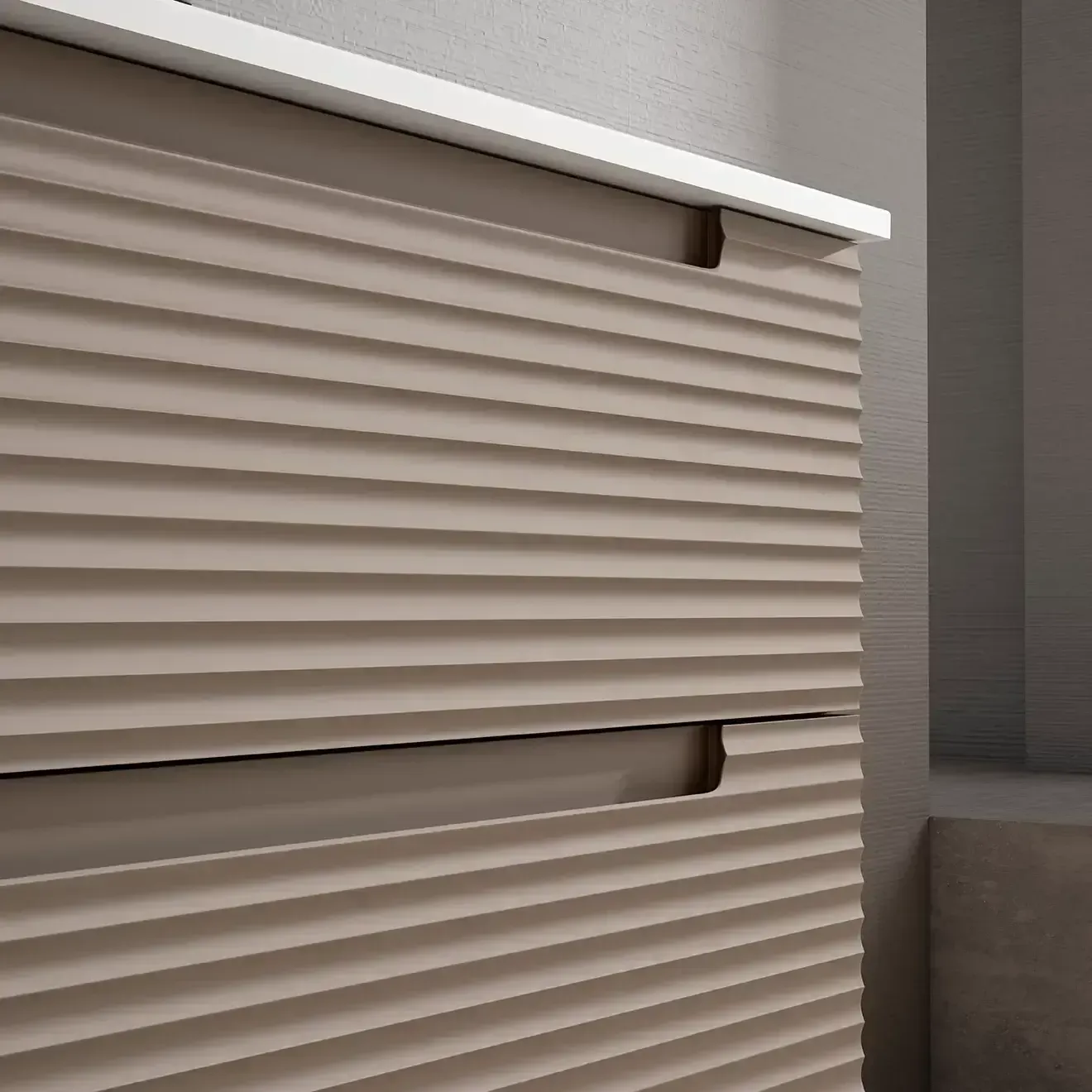 Primer plano de un armario de textura acanalada de color topo con dos cajones y una cubierta blanca contra una pared gris.