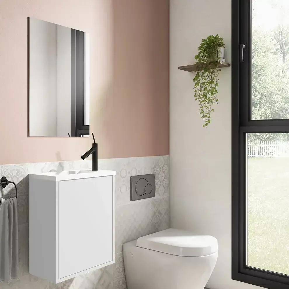 Baño moderno con tocador blanco, grifo negro, espejo e inodoro. Paredes rosas y blancas, ventana y plantas.