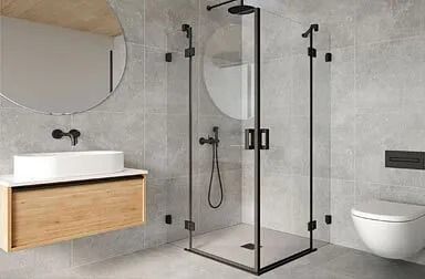 Baño moderno con ducha con marco negro, tocador flotante de madera, espejo circular, paredes grises y un inodoro blanco.