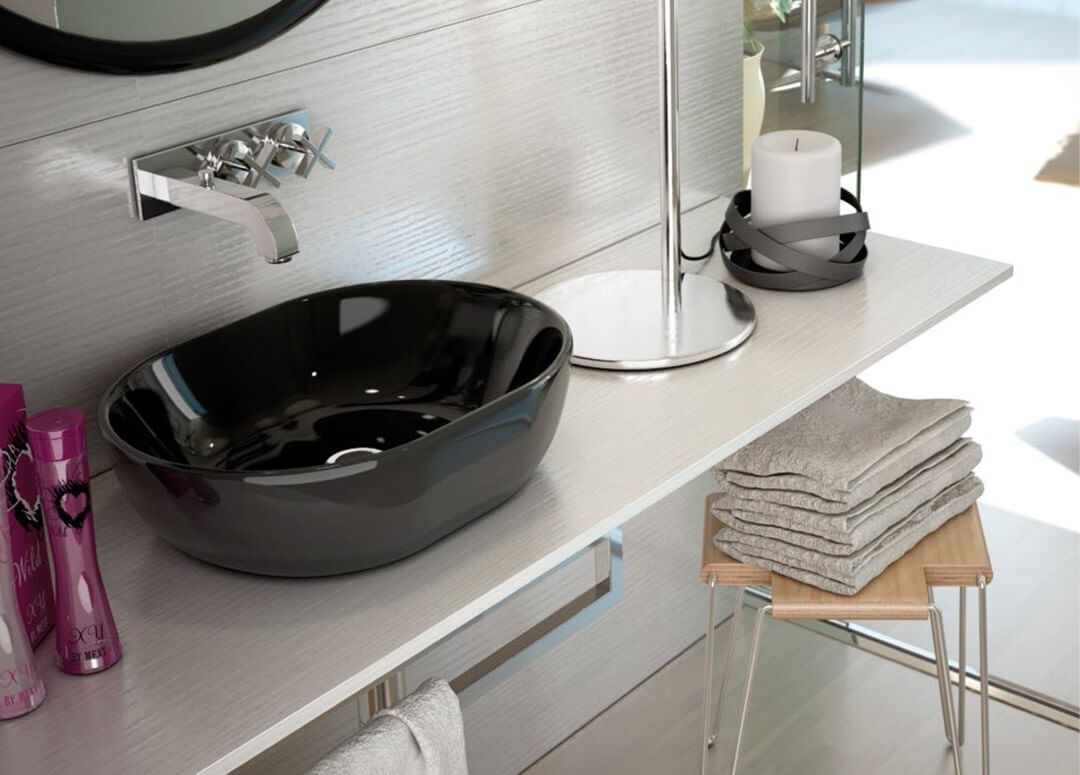 Lavabo ovalado negro sobre encimera blanca en baño moderno con grifo y accesorios cromados.