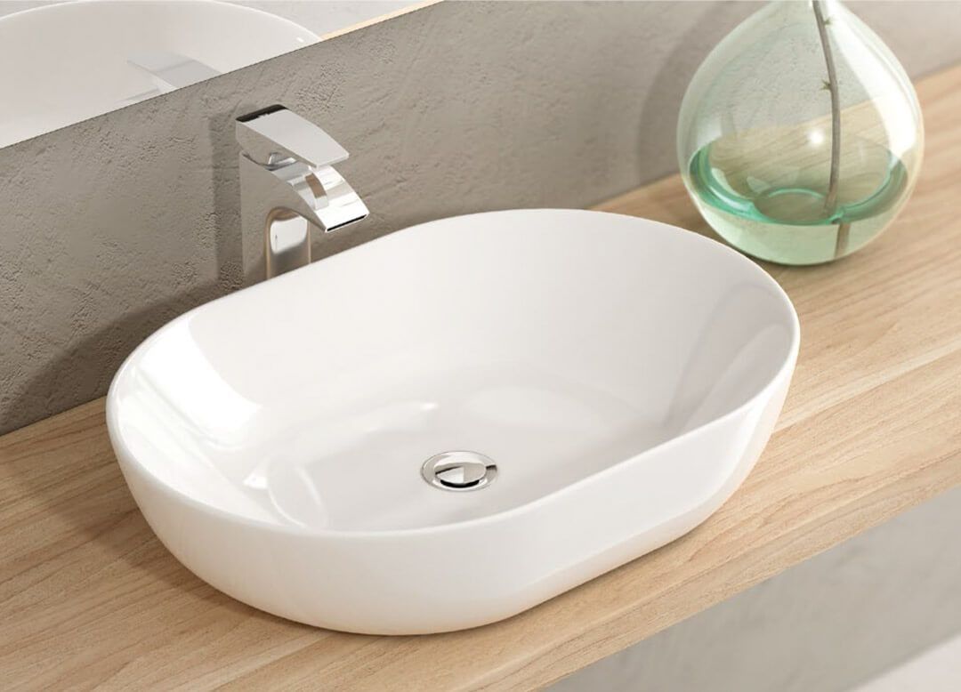 Lavabo de baño ovalado blanco sobre encimera de madera con grifo cromado y adorno de cristal.