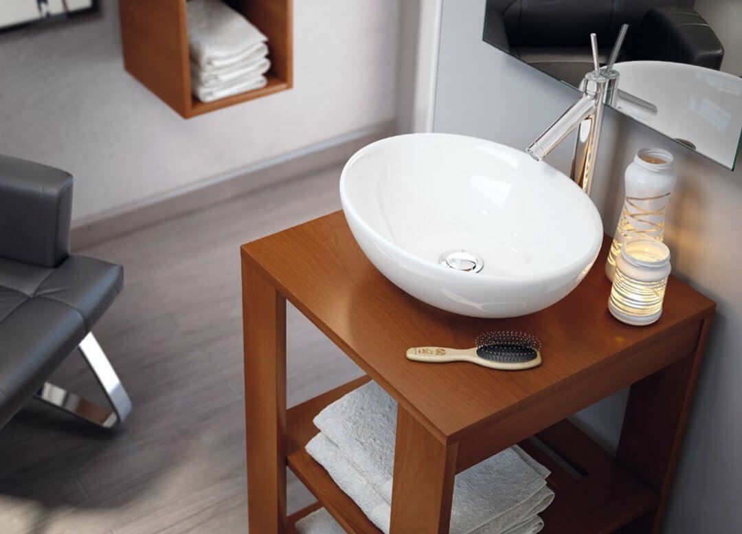 Lavabo blanco sobre soporte de madera marrón en un baño, con un toallero y una vela encendida.