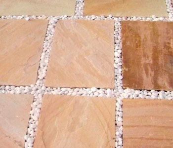 Pavimentos cuadrados de piedra beige con relleno de grava blanca.