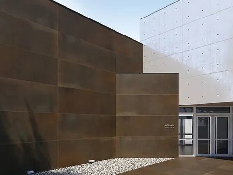 Exterior de un edificio moderno con paredes marrones y blancas. Entrada con puertas de cristal.