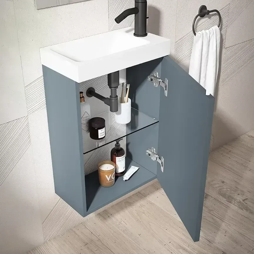 Mueble de baño azul con puerta abierta, lavabo, grifo y artículos de aseo. Toalla en un aro.