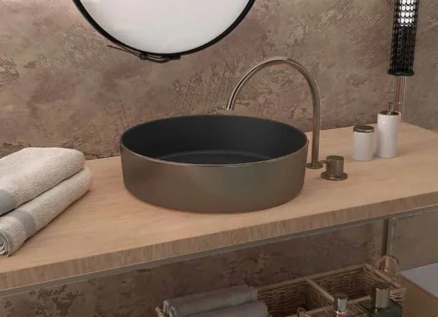 Lavabo de baño con pila redonda de color gris oscuro y grifo curvo, colocado sobre una encimera de madera clara.