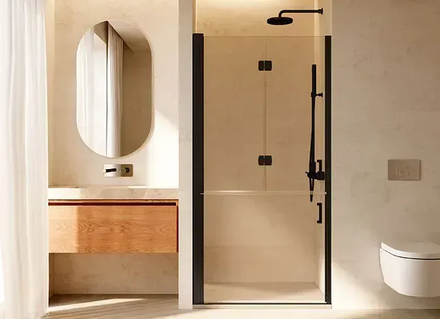 Baño moderno de color beige con ducha, inodoro, tocador de madera y espejo ovalado.