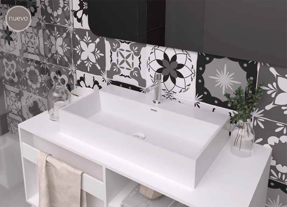 Lavabo rectangular blanco sobre una encimera blanca con salpicadero de azulejos estampados en gris y blanco.