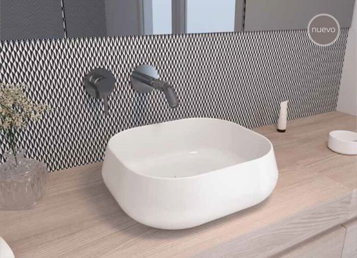 Lavabo blanco sobre encimera de madera con grifo de pared. Salpicadero con estampado oscuro.
