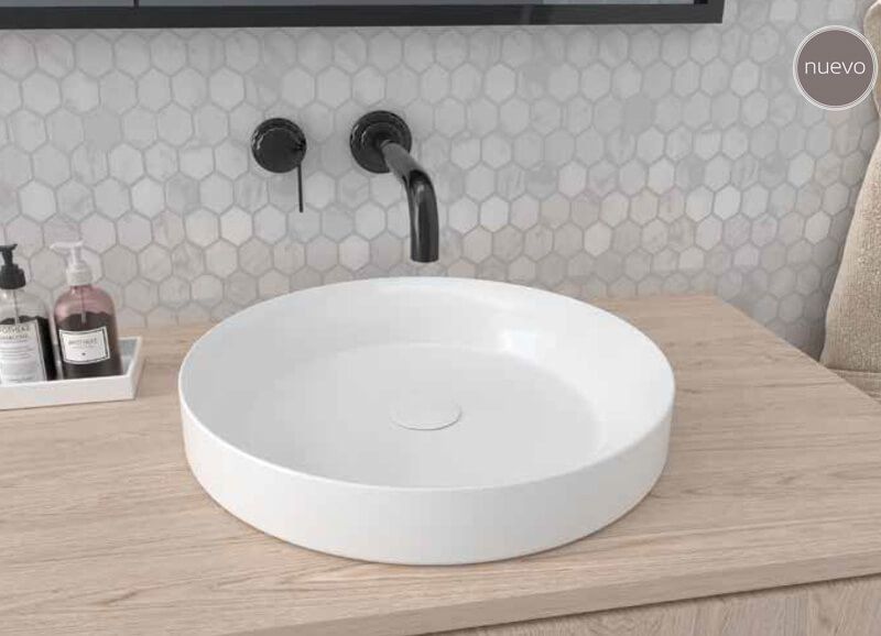 Lavabo circular blanco sobre tocador de madera con grifo negro y pared de azulejos grises.