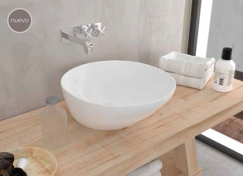 Lavabo blanco sobre tocador de madera en un baño con toallas, grifo y artículos de tocador.