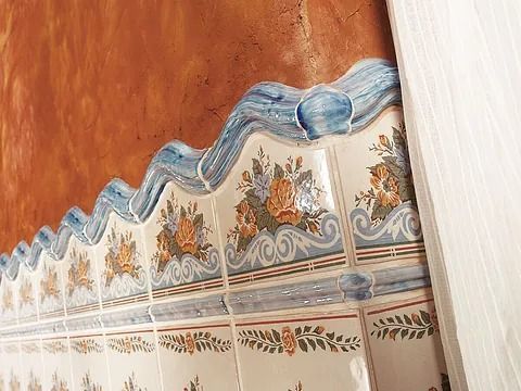 Azulejos con estampado floral y borde ondulado azul sobre una pared naranja.