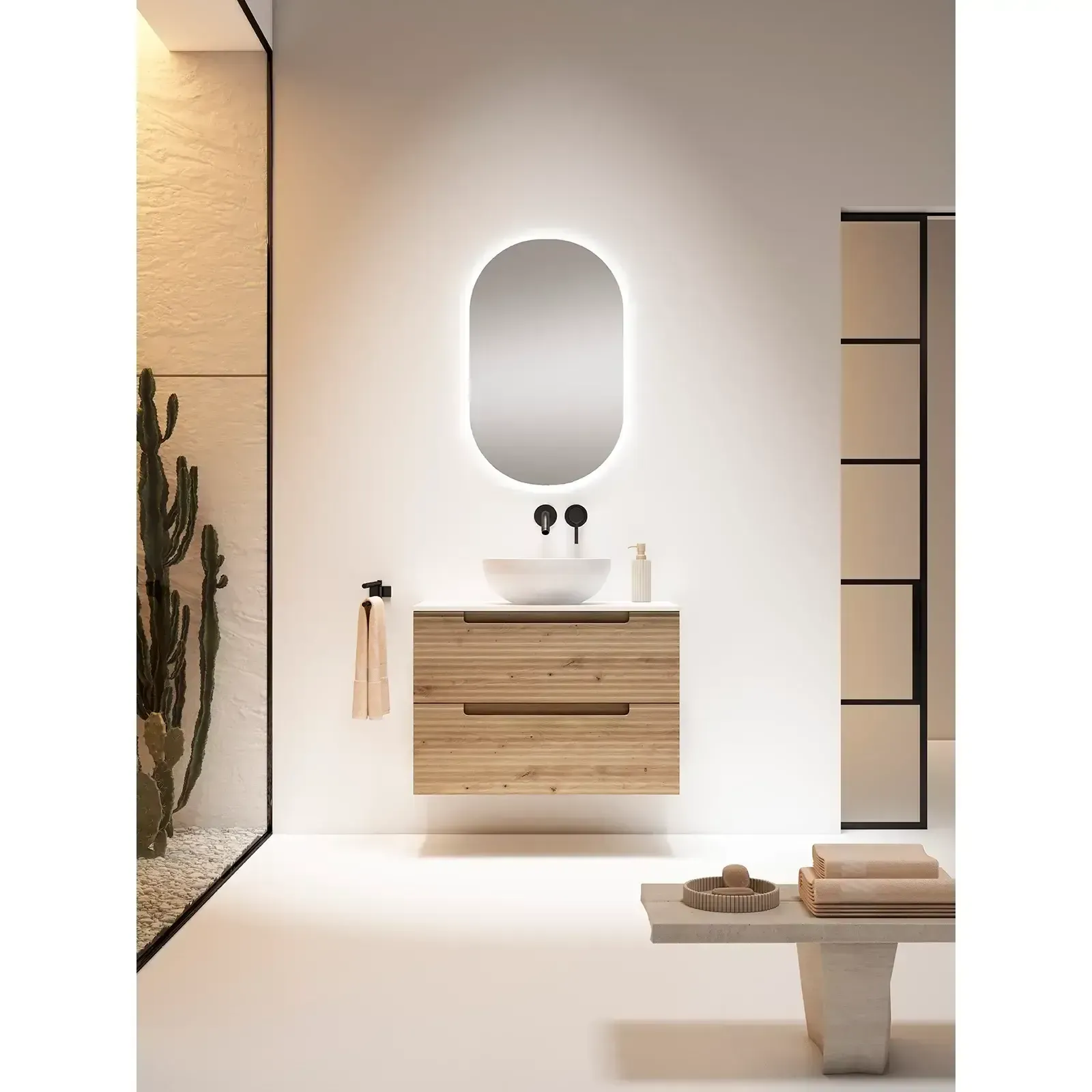 Baño moderno con tocador de madera, espejo ovalado con iluminación de halo y cactus.