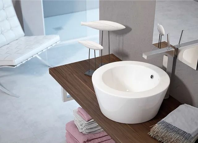 Baño moderno con lavabo de pedestal blanco sobre encimera de madera, esculturas de pájaros decorativas, silla blanca y toallas.