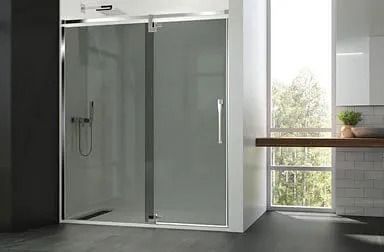 Mampara de ducha con puerta corredera, marco cromado y paneles de vidrio esmerilado. Ambiente de baño con luz natural.