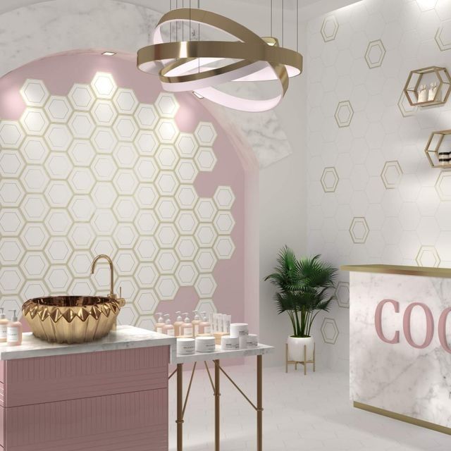 Interior de spa con decoración en rosa, dorado y blanco: azulejos de pared hexagonales, lavabo y mostrador de recepción.