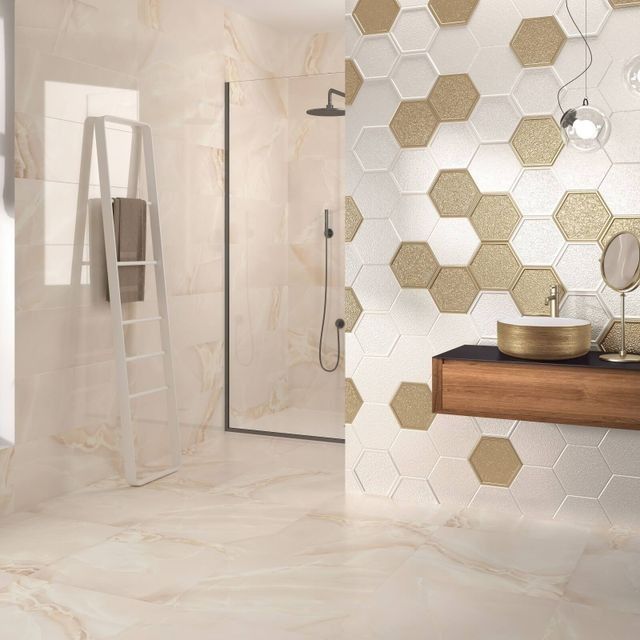 Baño moderno con paredes y piso de mármol beige, ducha y una pared con acento hexagonal blanco con azulejos dorados.