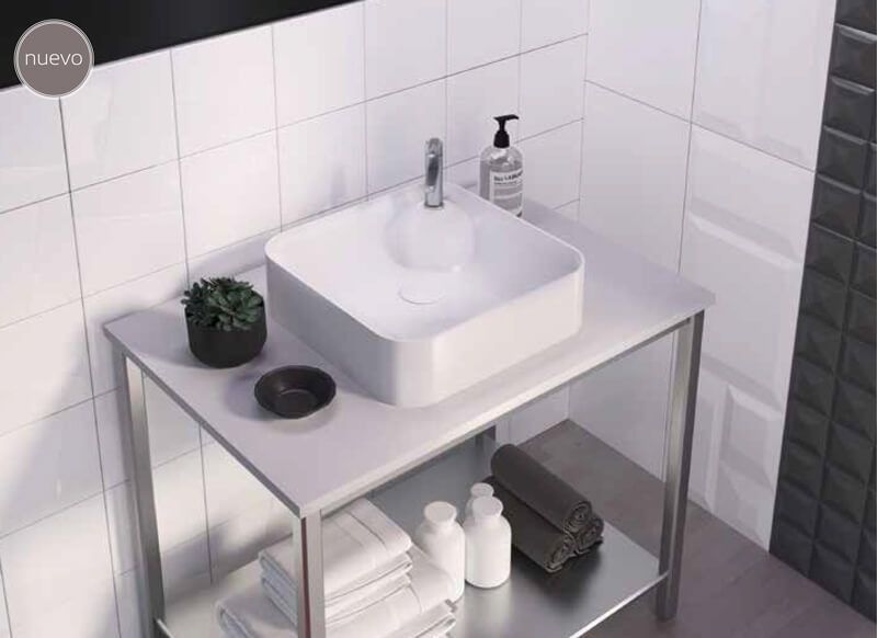 Lavabo cuadrado blanco sobre soporte de metal, situado en un baño alicatado, con toallas y artículos de aseo.