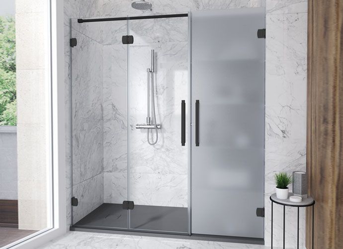 Cabina de ducha con puertas de vidrio transparente y esmerilado, herrajes negros, azulejos grises y una pequeña mesa auxiliar.