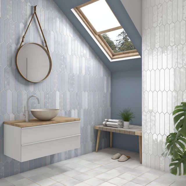 Baño con paredes azules, azulejos con diseño ovalado, tragaluz, tocador flotante con espejo redondo.